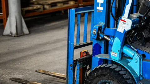 Blauer Gabelstapler in einem Industrie-Lager, geparkt in der Nähe von Regalen mit verschiedenen Gegenständen.